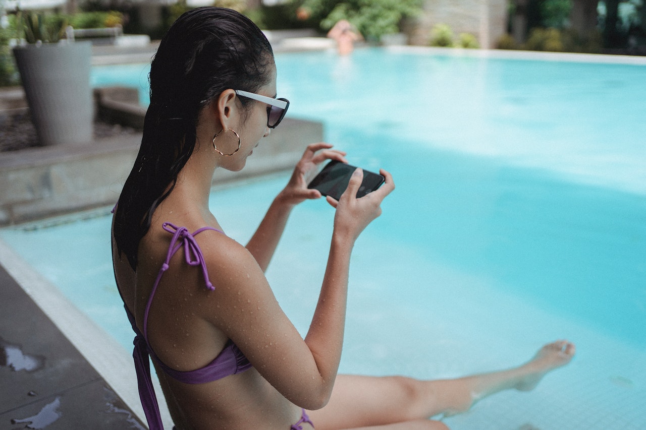 Jeune femme au bord d'une piscine avec son téléphone ©Pexels